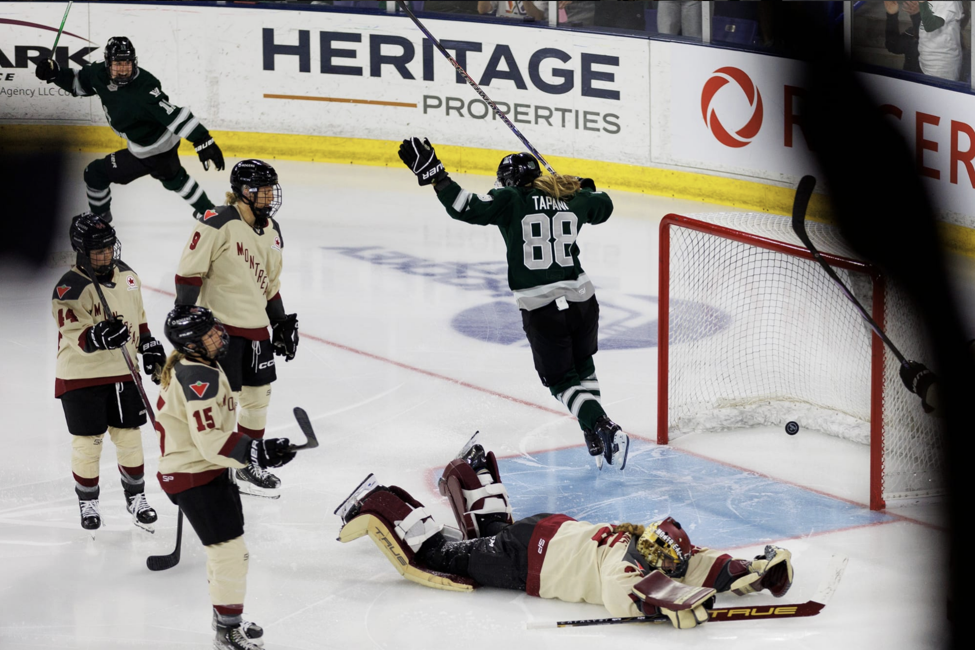 Tapani raises her arms in celebration as she skates through the crease, as Desbiens lays flat on her stomach outside the crease following a desperation dive. Three Montréal players are staring solemnly at the net.
