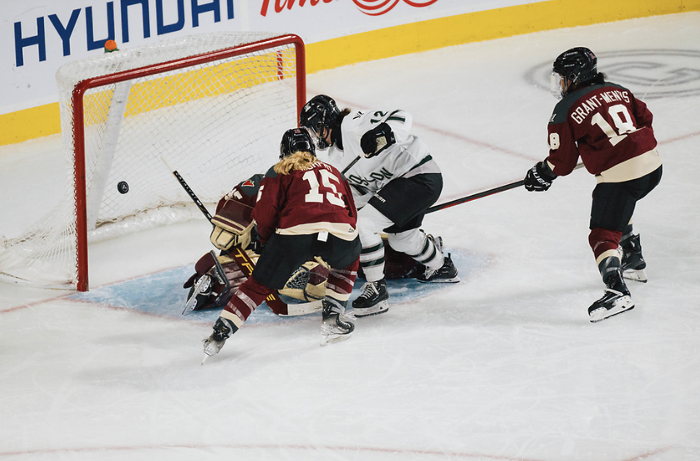 Wenczkowski scores from just outside the crease. Two Montréal players are trying to defend while Desbiens is on her knees and mostly blocked from the shot. Wenczkowski is in white, while the Montréal players are in maroon.