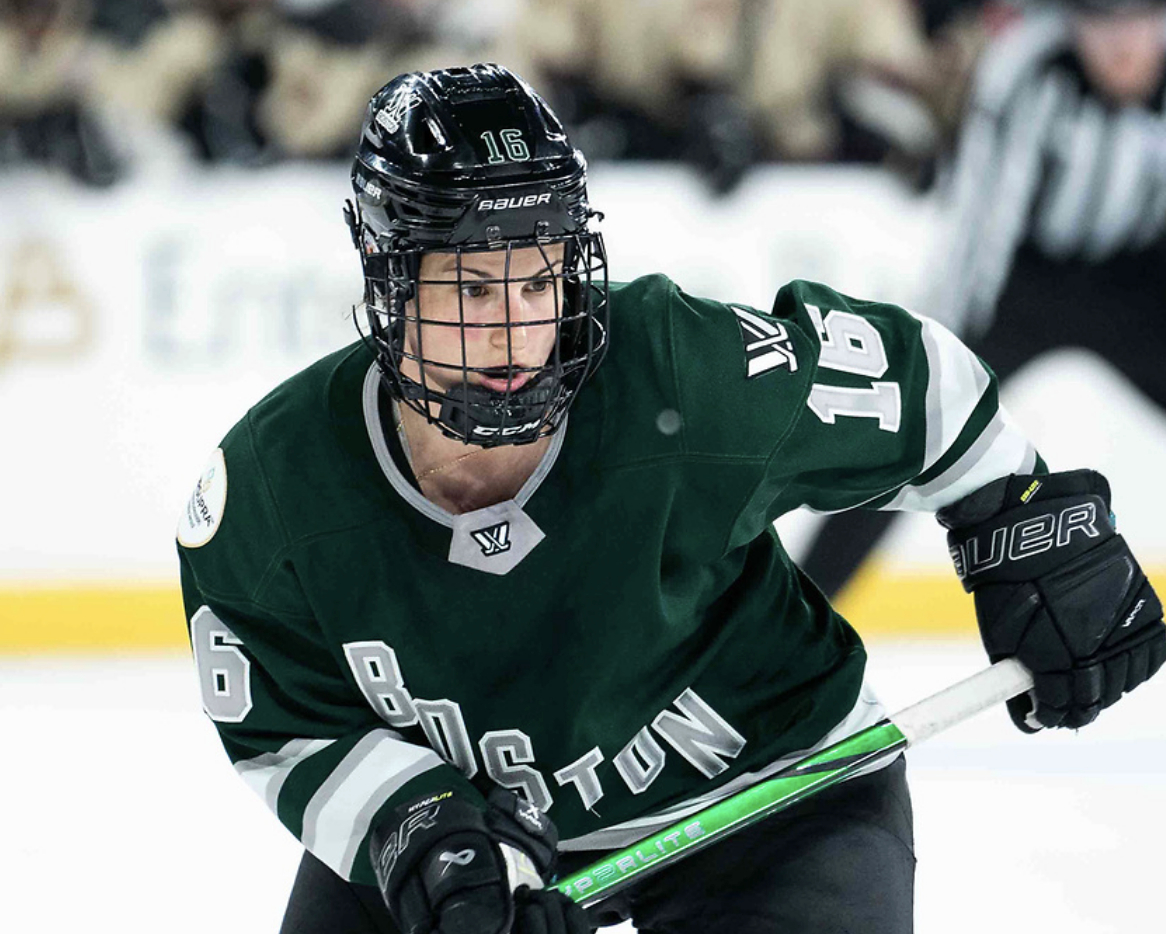 Pelkey is slightly crouched, watching a play to her left. She has both hands on her stick and is wearing a green home uniform.