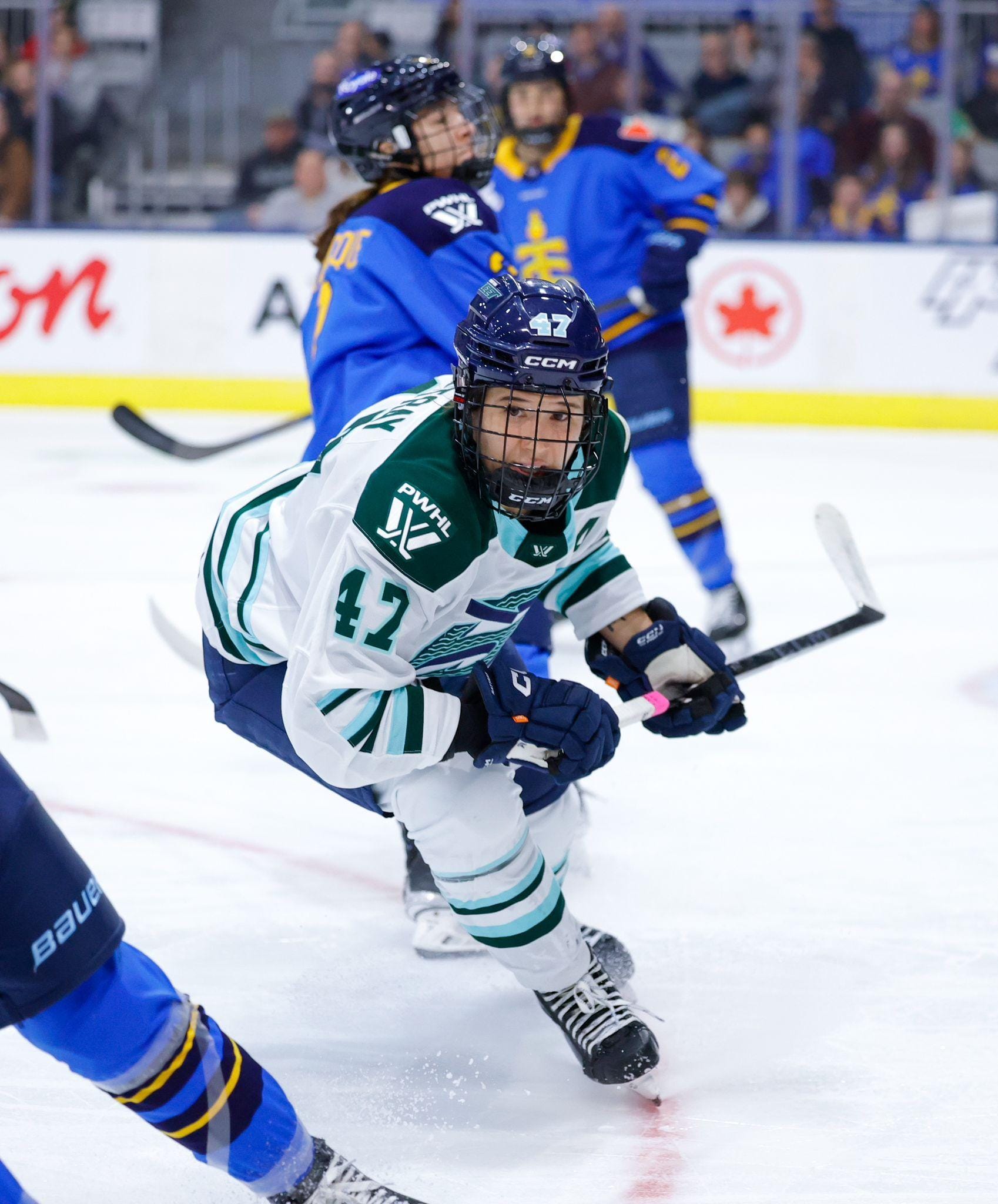 Rattray is mid-turn, looking towards the puck which is out of frame. She is leaning forward with her stick at waist level and wearing a white away uniform.