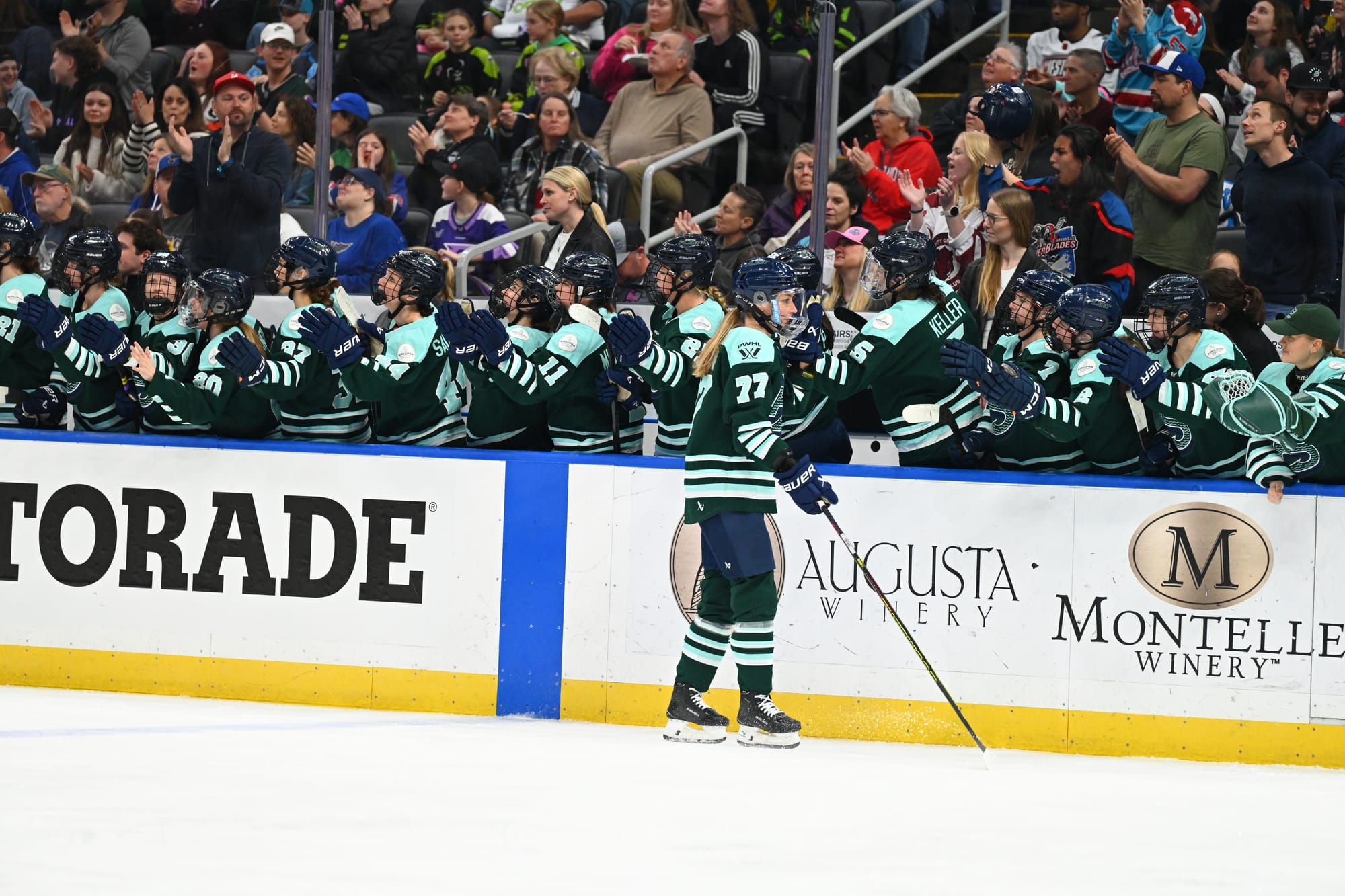 Tapani goes down the handshake line at the bench after scoring. She is wearing a green home uniform.