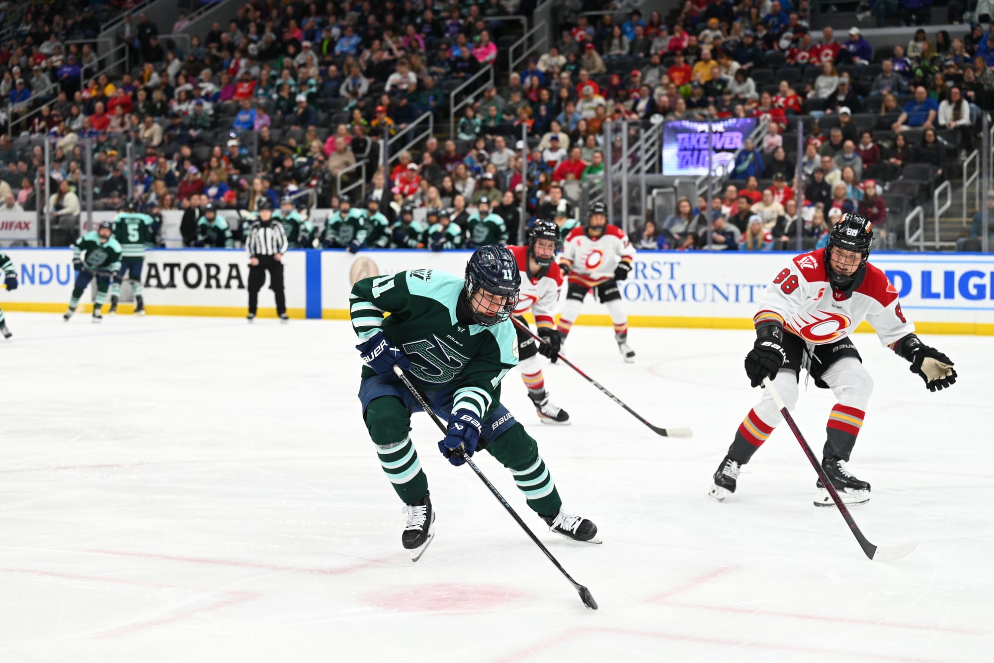 Müller looks down at the puck as she uses her body to protect it against oncoming Ottawa defenders. She is wearing a green home uniform, while the Ottawa players are in white away ones.