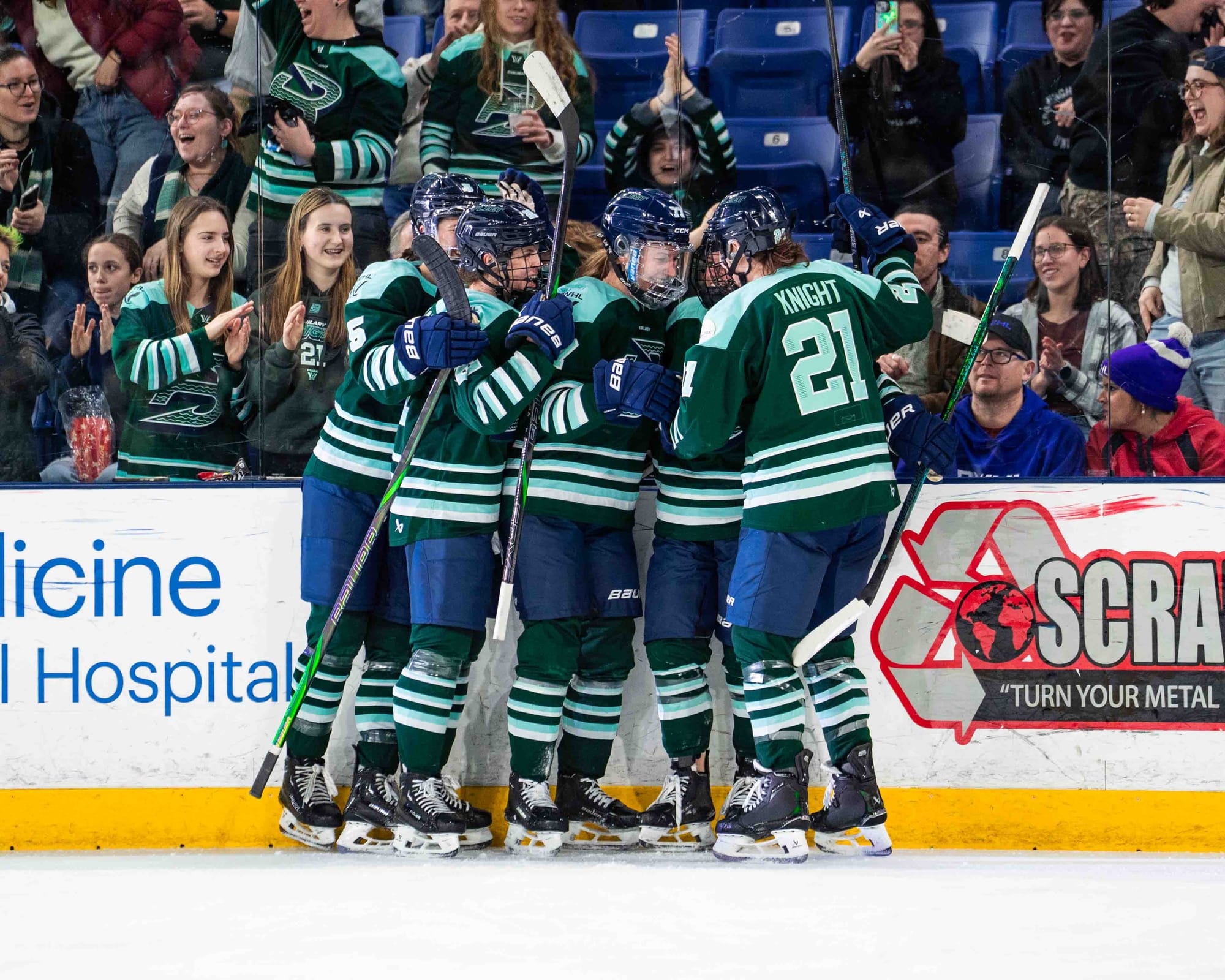Five Fleet players celebrate with a group hug along the boards. They are wearing green home uniforms.