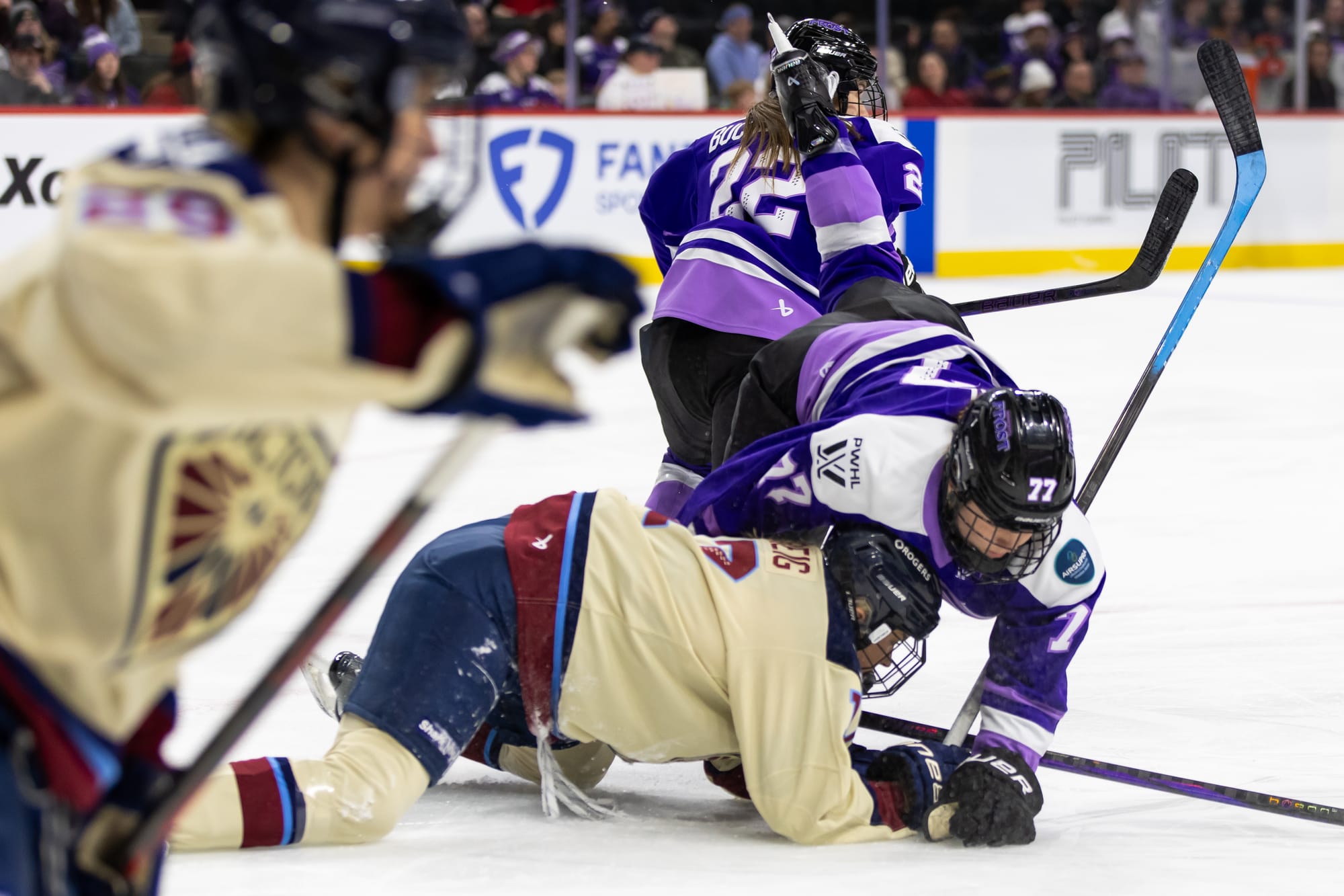 Curl-Salemme is falling to the ice with her arms outstretched. One of her legs is raised above her head. There is a Montréal player on the ice right in front of her. Curl-Salemme is in a purple home jersey, while the Montréal player is in a cream away one.