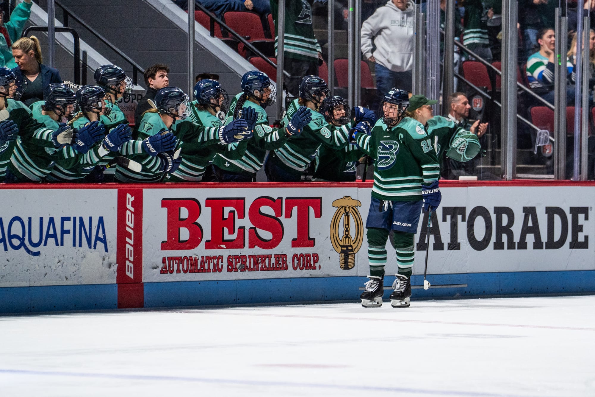 Knight skates down the handshake line at the bench to celebrate her goal. She is wearing a green home uniform.