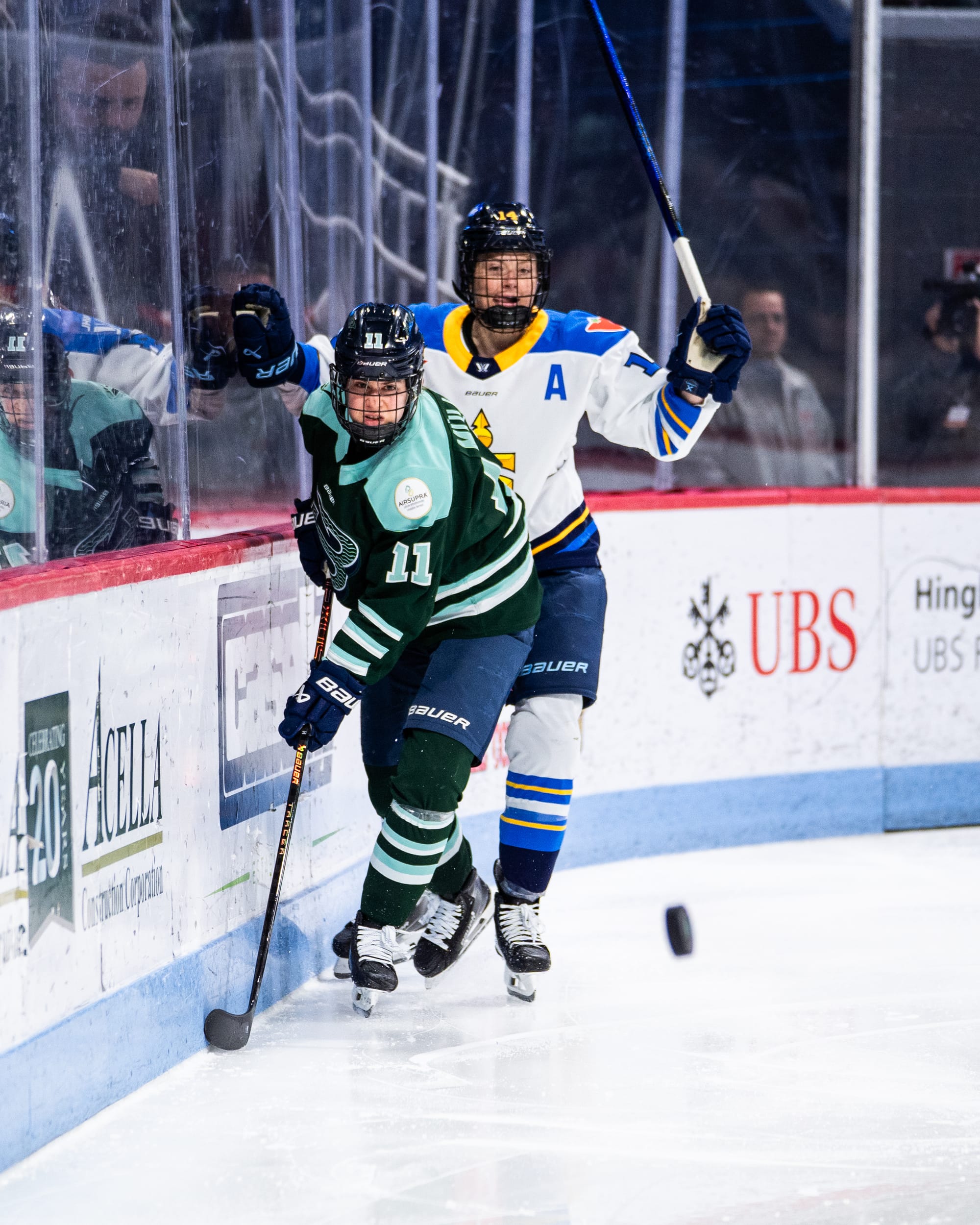 Müller (front in green) keeps her eye on the puck, which is ahead to her left. Fast (back in white) is pushing off from the battle to pursue the puck. 