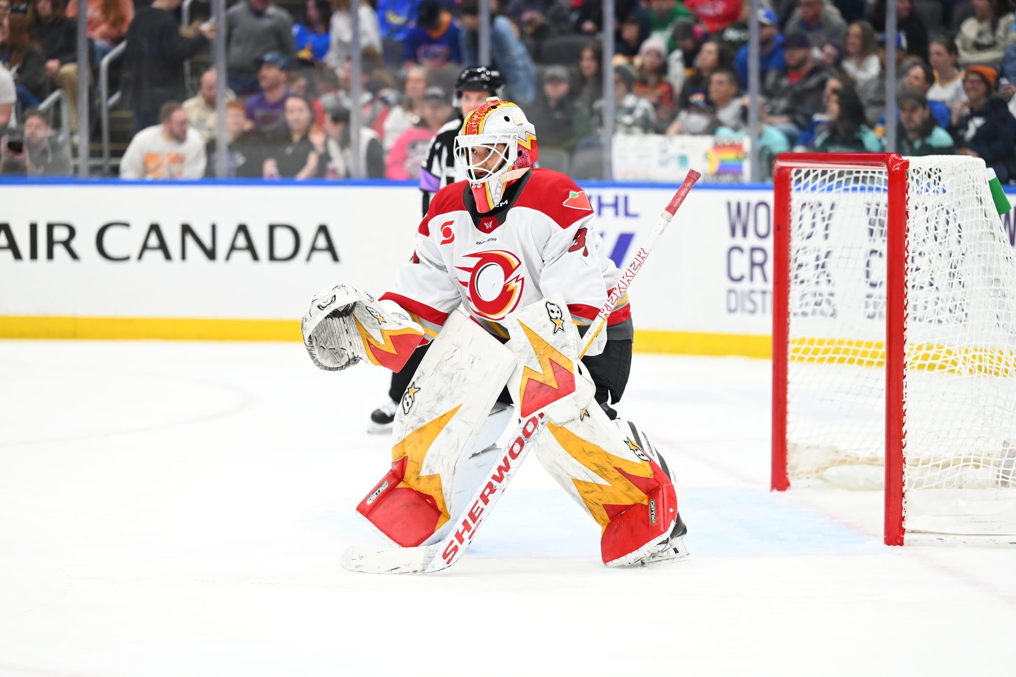 Phillips is at the top of her crease, crouched into the ready goalie position with her stick down and glove low. She is wearing a white away uniform.