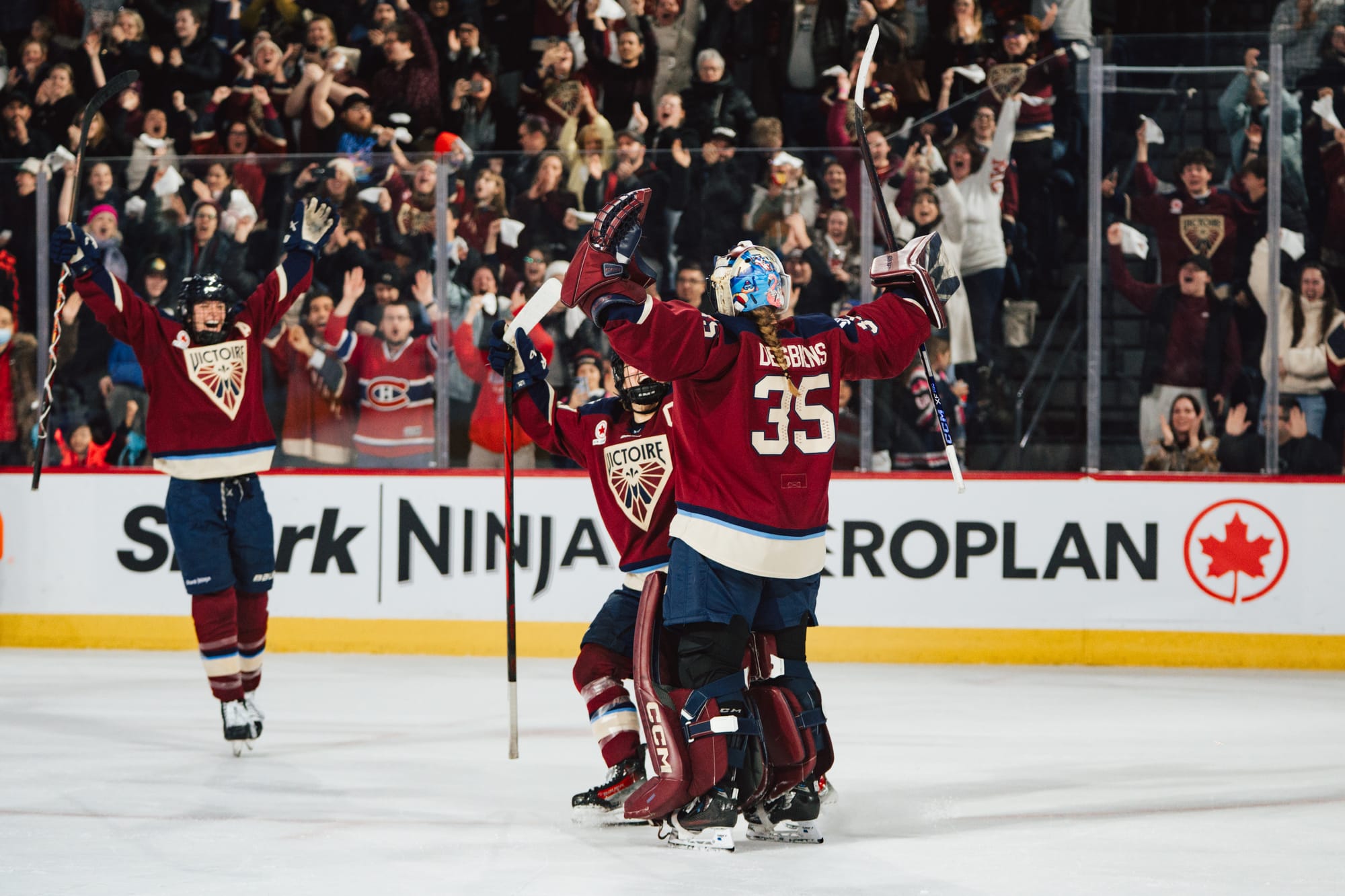 Three Montréal players celebrate a win with a group hug. They are wearing maroon home uniforms.