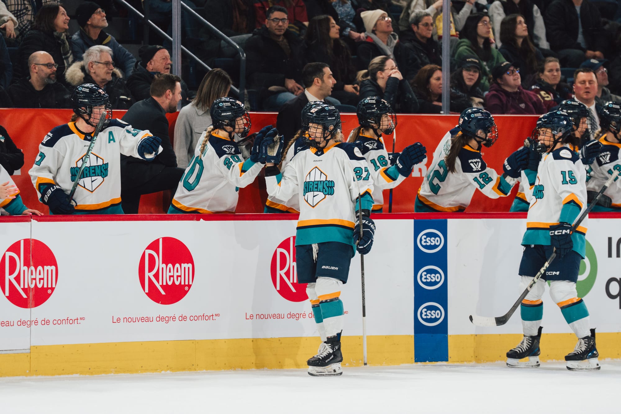 Downie-Landry goes down the handshake line at the bench to celebrate her goal. One of her teammates is behind her doing the same. They are all wearing white away uniforms.