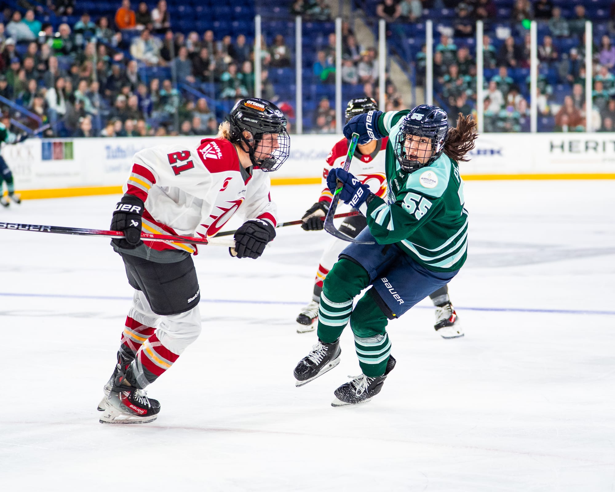 Pejšová (right in green) hunts the puck, as Bell (left in white) skates to defend her.