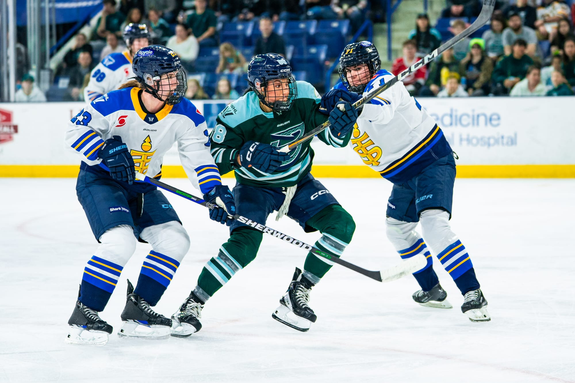Adzija (middle in green) tries to skate toward the middle of the ice, while Toronto players (wearing white) are on either side of her trying to slow her down.