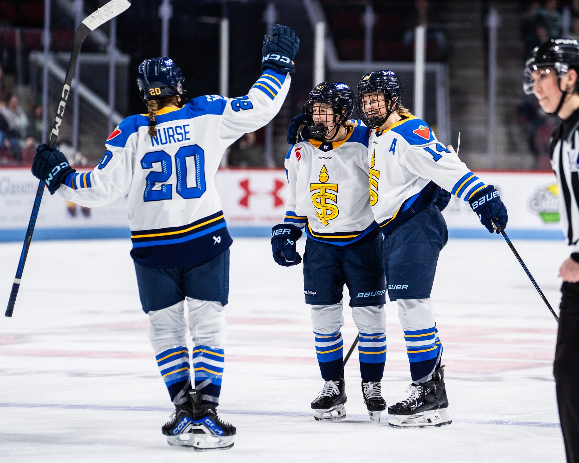 Three Toronto players celebrate with a group hug at the blue line. They are wearing white away uniforms.