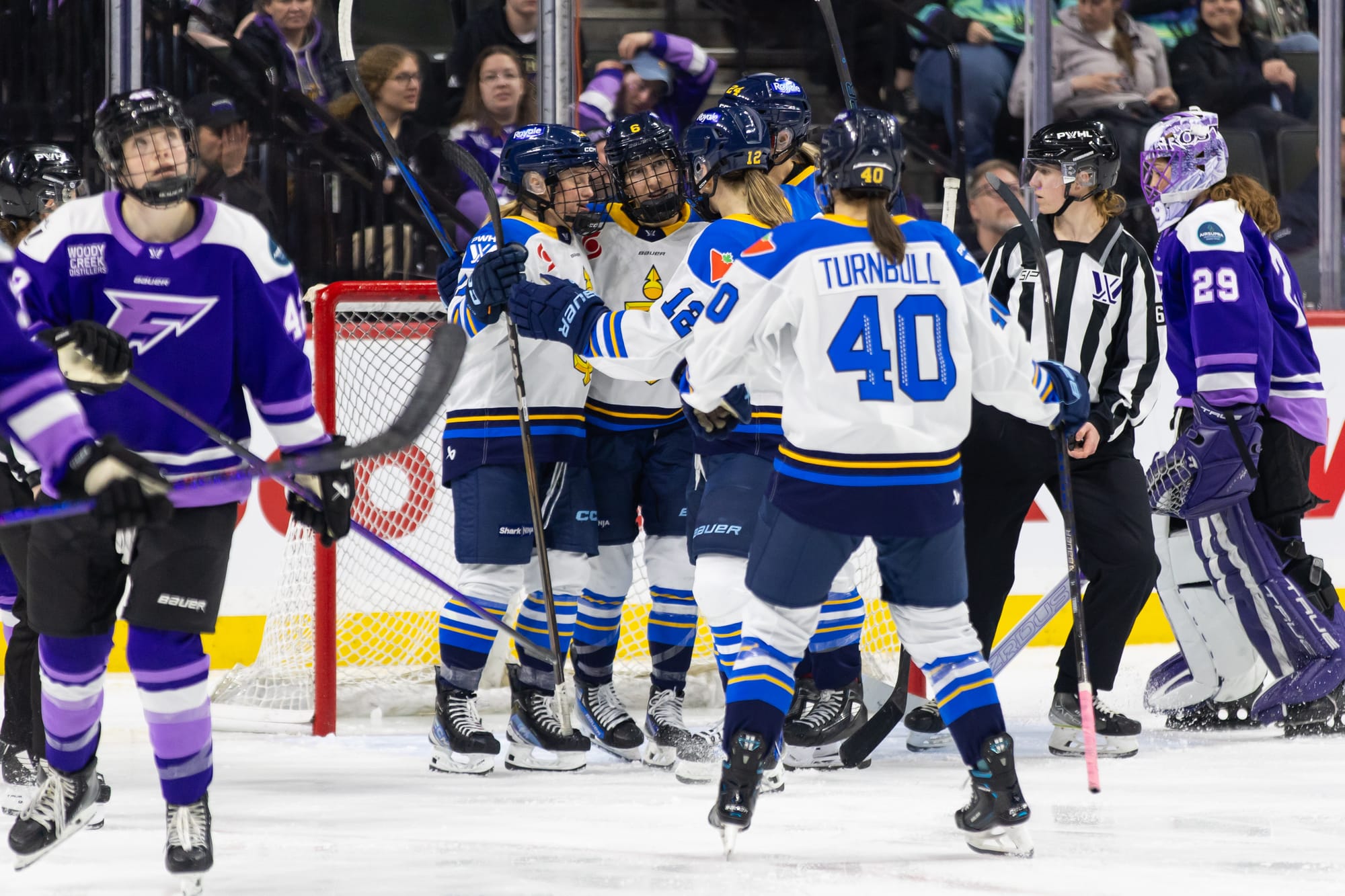 Toronto players celebrate a goal with a group hug in front of the crease. They are wearing white away uniforms.