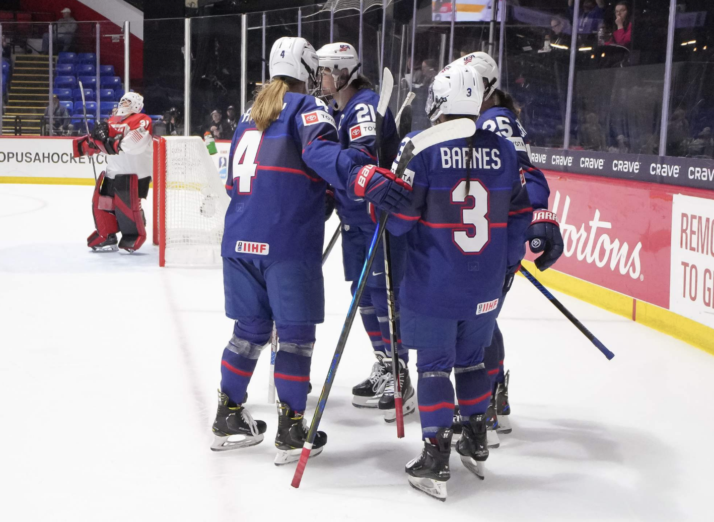 U.S. players celebrate a goal with a group hug in the corner. They are wearing blue uniforms.