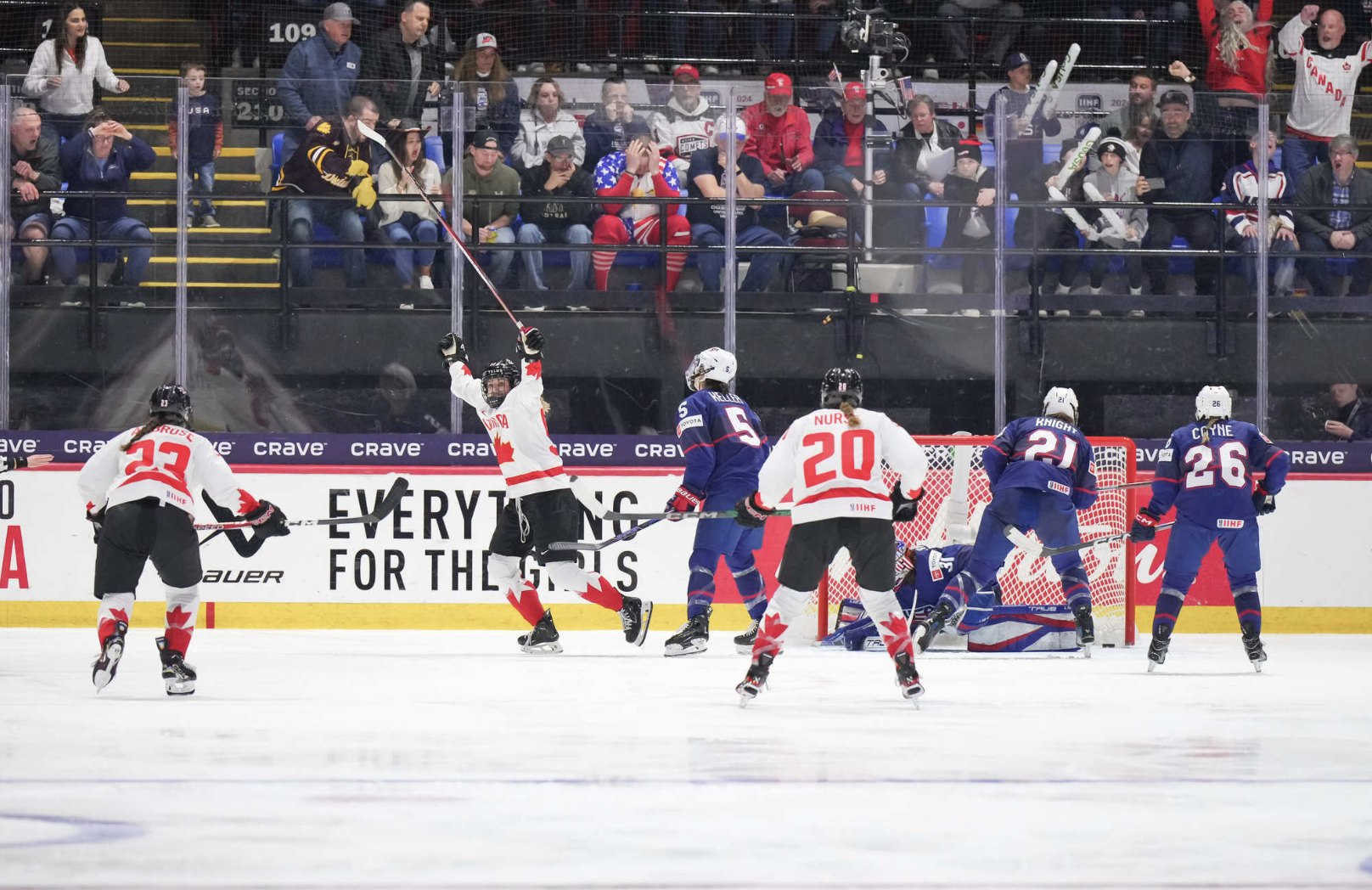 Three Canada players celebrate the winning goal, while three U.S. skater and Aerin Frankel look on in disappointment. The Canadian players are wearing white uniforms, while the Americans are in blue.