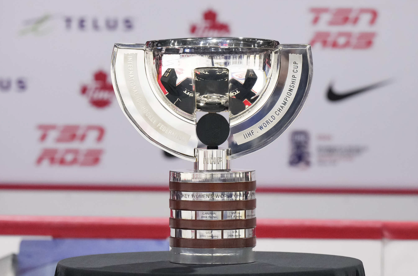 A silver trophy with a cup on top, and then rings of engraved plates that feature the winning country. There is a puck in the center of the trouphy.