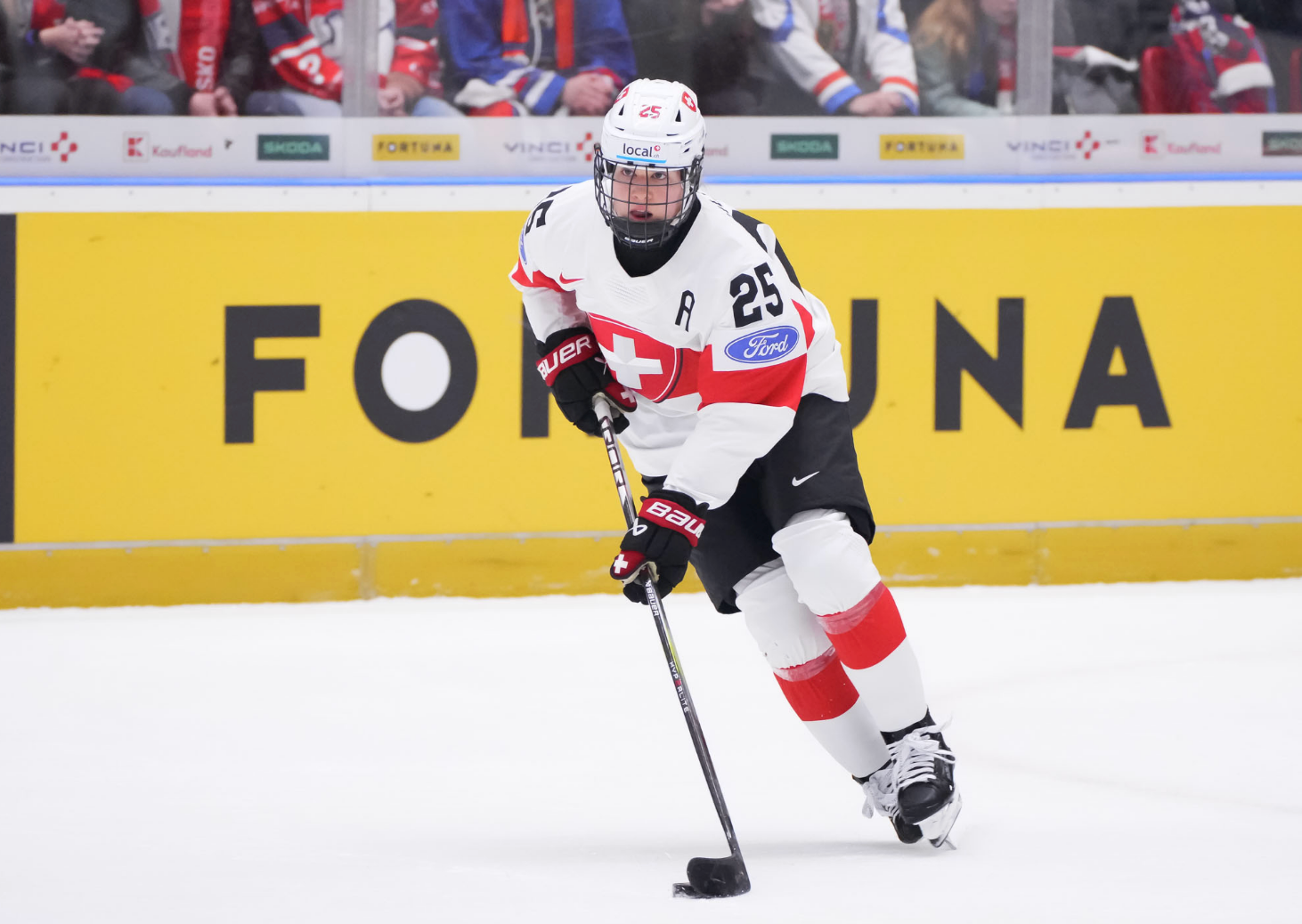Müller looks up as she skates out of the zone with the puck. She is wearing a white uniform.