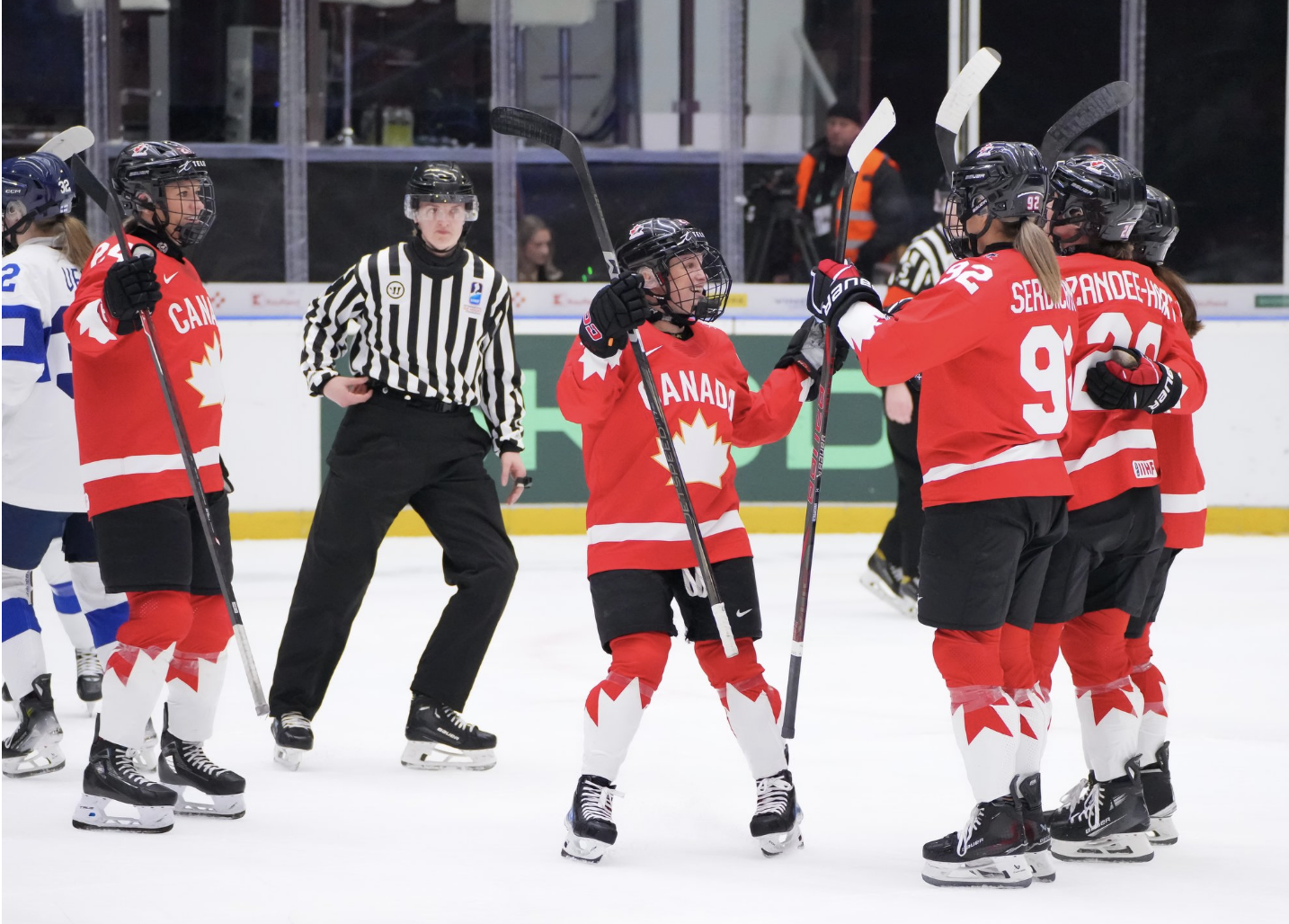 Five Canada players celebrate a goal with a group hug. They are wearing red uniforms.