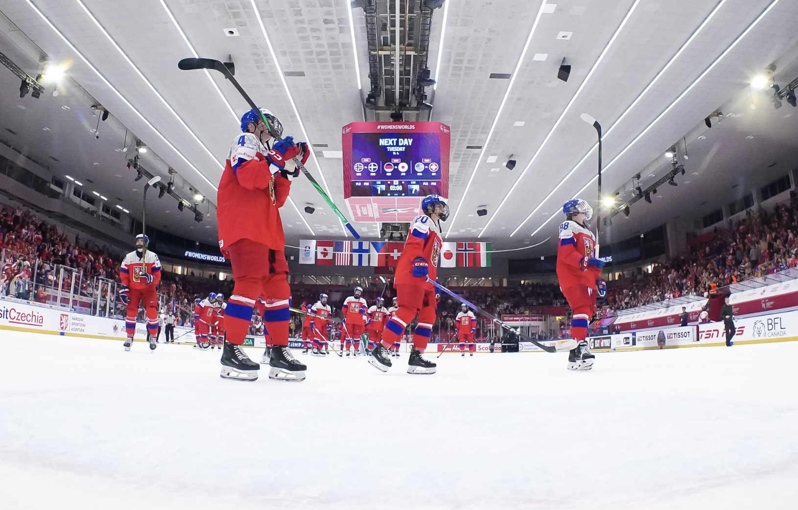 Czechia players skate around, saluting their home crowd. They are wearing red uniforms.