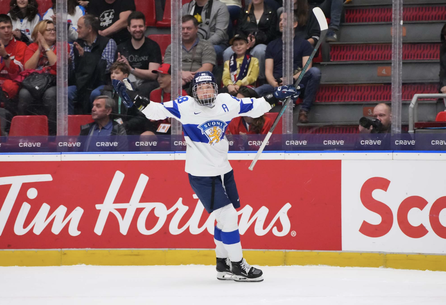 Savolainen raises her arms in celebration, waiting for her teammates to arrive for a hug. She is wearing a white uniform.