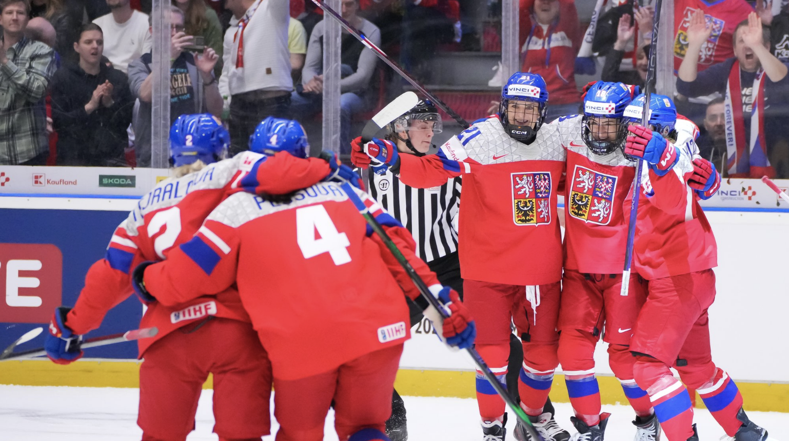 A pair of hugging Czechia players skates toward a trio of hugging players to celebrate a goal. They are all wearing red uniforms.
