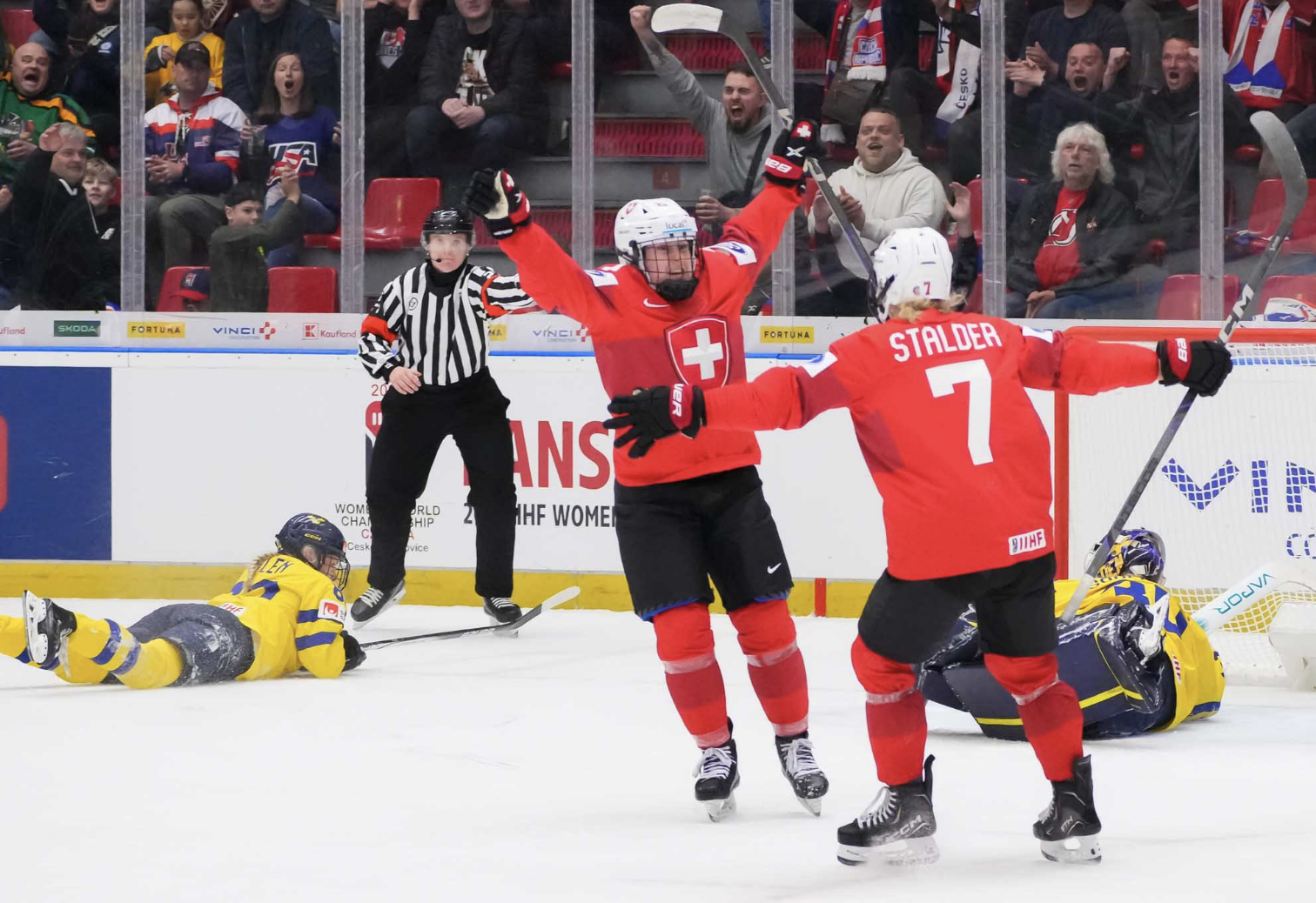 Two Switzerland players skate toward each other with wide open arms for a hug, while a Sweden skater and Söderberg lay on the ice. The Swiss players are in red, Sweden in yellow.