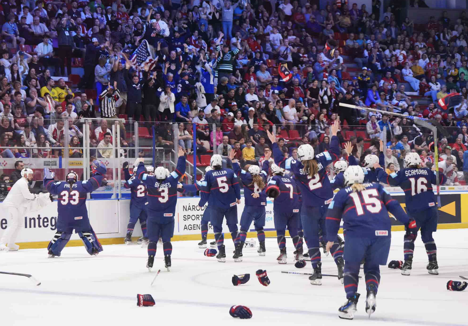 Team USA skates to the glass under where their family and friends are sitting to celebrate their gold medal win. They are all wearing blue uniforms.