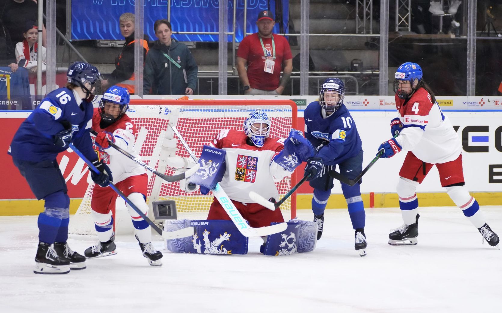 Peslarová is down on her knees making a save. Tejralová is off to her right, Pejšová to her left, and each are battling a Finland player. The Czechs are wearing white, while Finland is in blue.