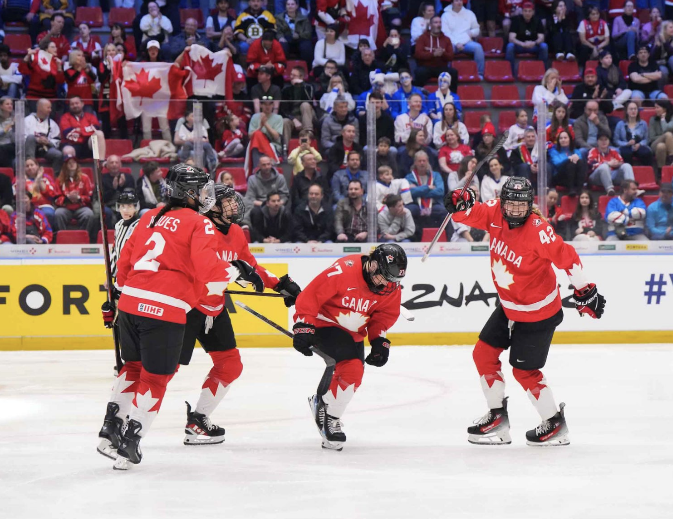 Emma Maltais pumps her fist in celebration as three teammates begin to surround her for a group hug. They are all wearing red uniforms.