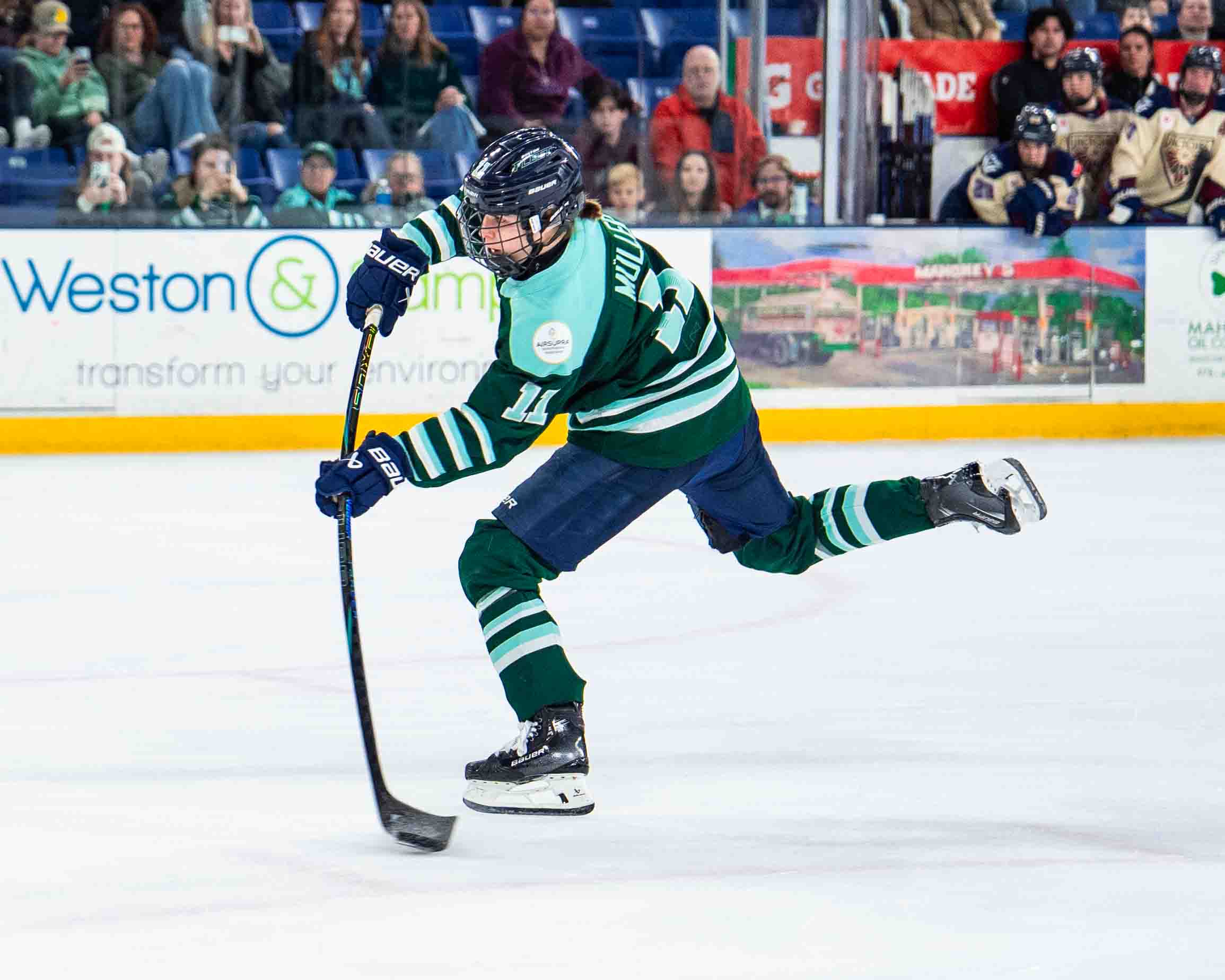 Müller shifts all her weight to her left (front) leg as she takes a wrist shot. She is wearing a green home uniform.