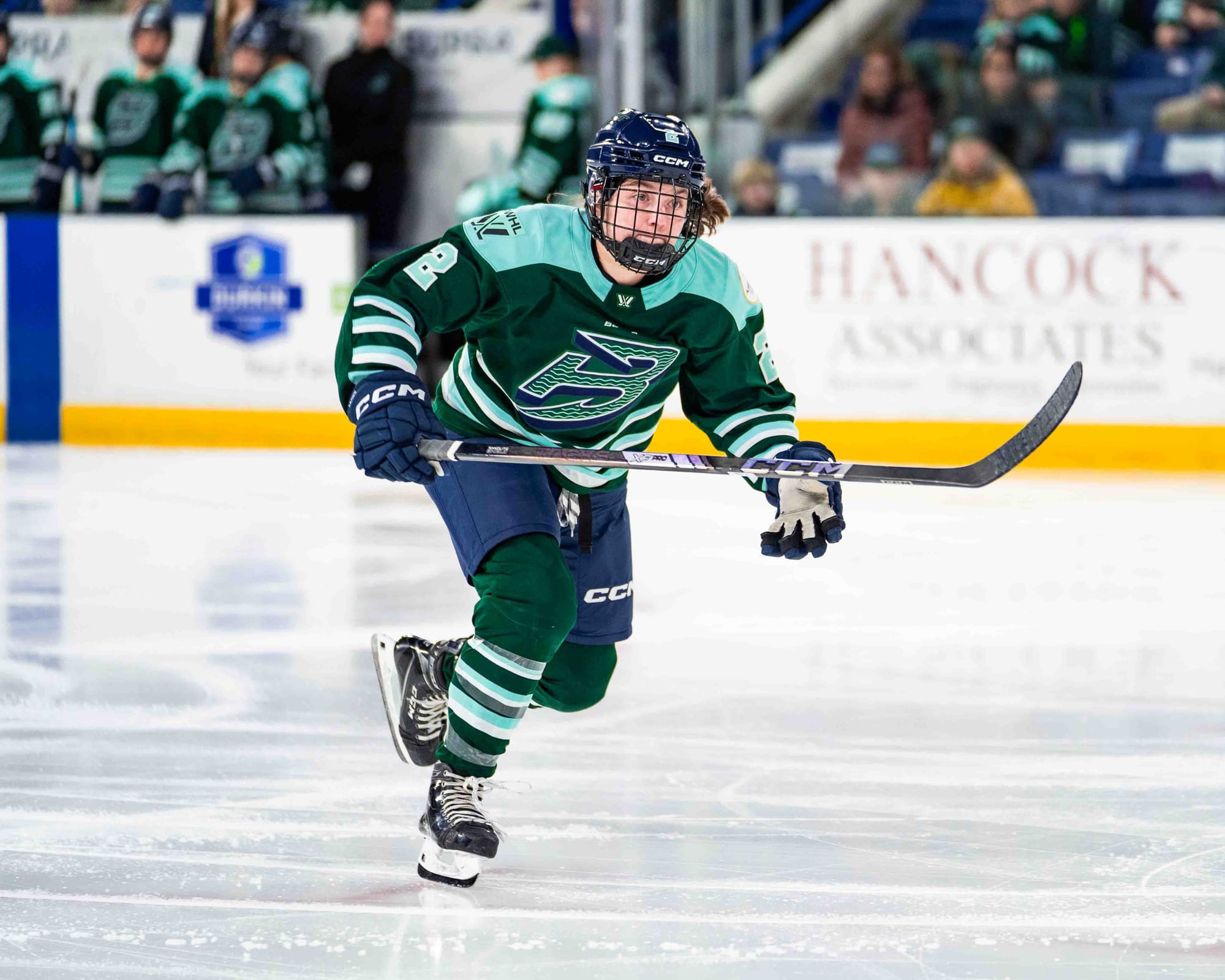 Brown skates down the ice, presumably toward a play. She is wearing a green home uniform.