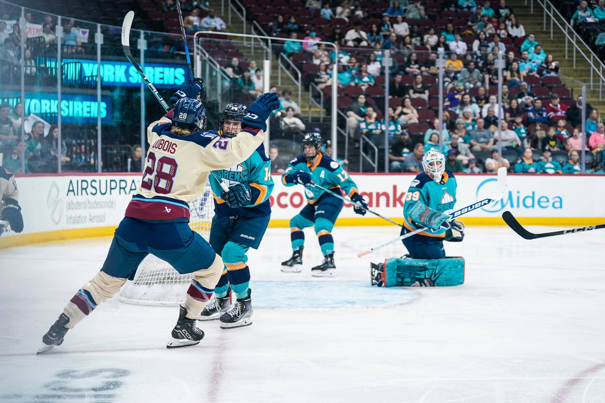 Duboise raises her arms in celebration as New York players look on in disappointment. She is wearing a cream away uniform, while the New York players are in teal home ones.