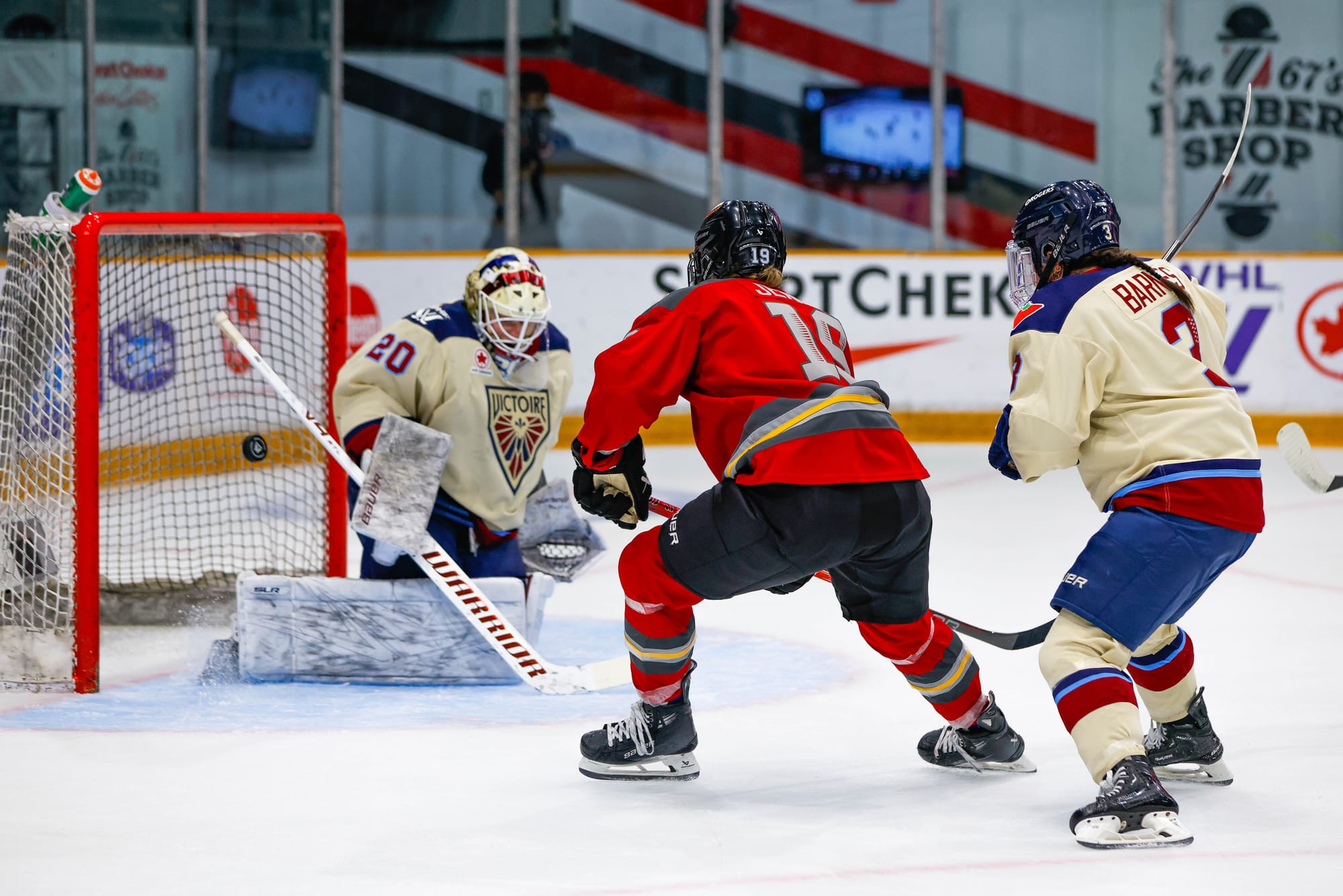 Jenner stops just outside the crease as the puck sails past a kneeling Chuli. Cayla Barnes is chasing after Jenner, who is wearing a red home unifom. The Montréal players are in cream away ones.