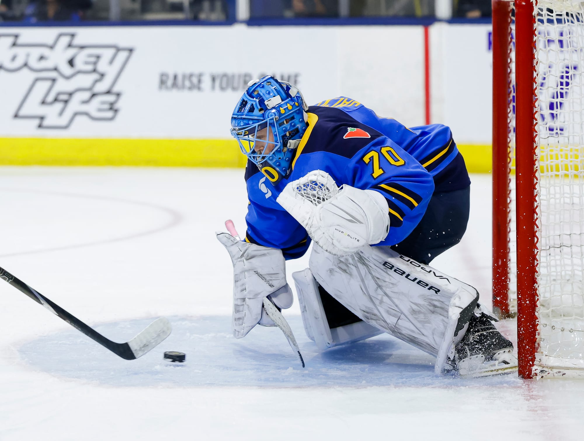Jackson crouches, with their glove hand pulled back as they prepare to clamp down on the puck. Only the stick of the Sirens player is visible on the left side of the screen. Jackson is wearing a blue home uniform.