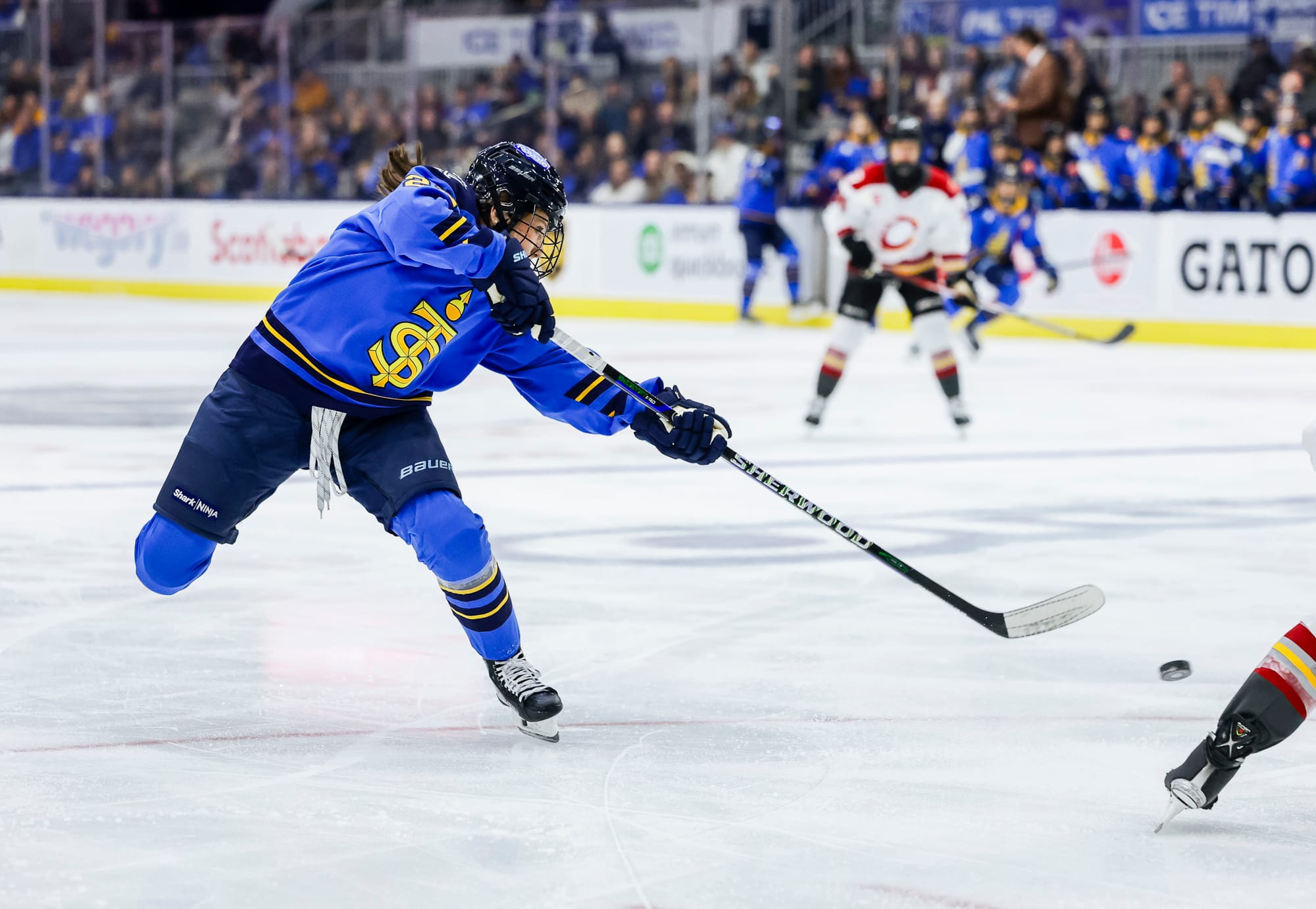 A Toronto player lifts her leg and leans forward and to her left, into the follow through of her shot. She is wearing a blue home uniform.