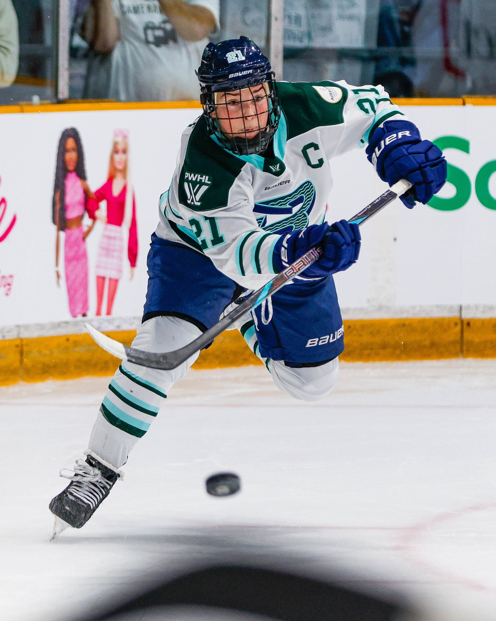 Knight looks forward and lifts her left leg as she fires the puck up ice. She is wearing a white away uniform.