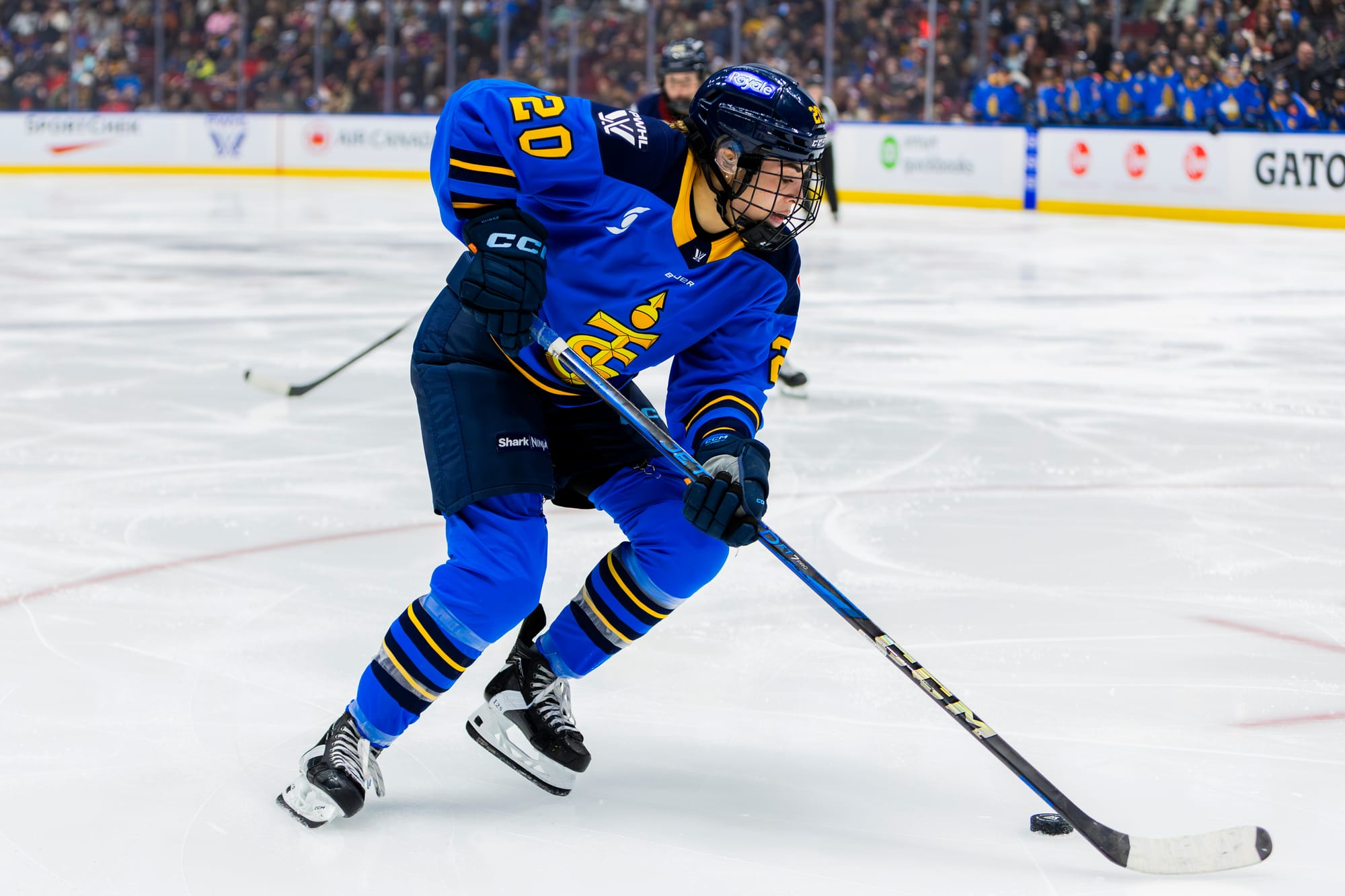 Nurse is skating, using her body to shield the puck in one of the face-off circles. She is wearing a blue home uniform.