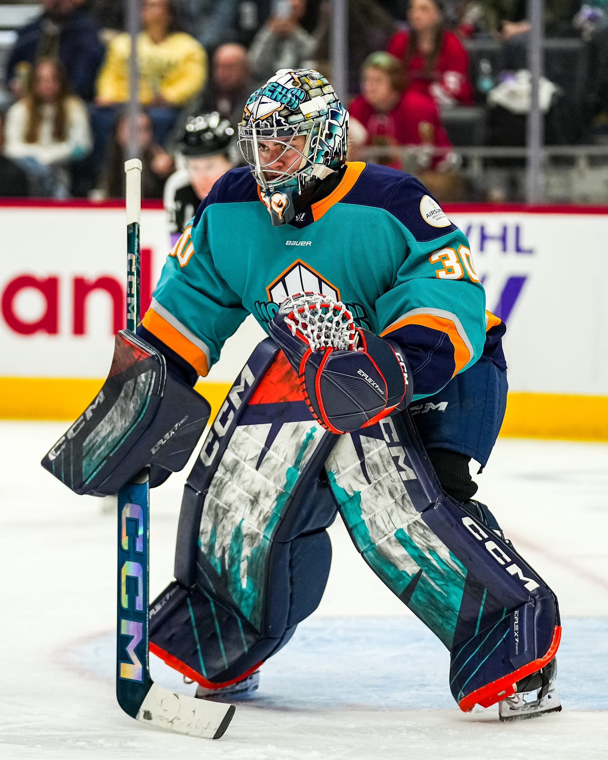 Schroeder crouches with her stick on the ice as she watches the face-off circle, which is out of the frame, intently. She is wearing a teal home uniform to come along with her New York skyline style pads.