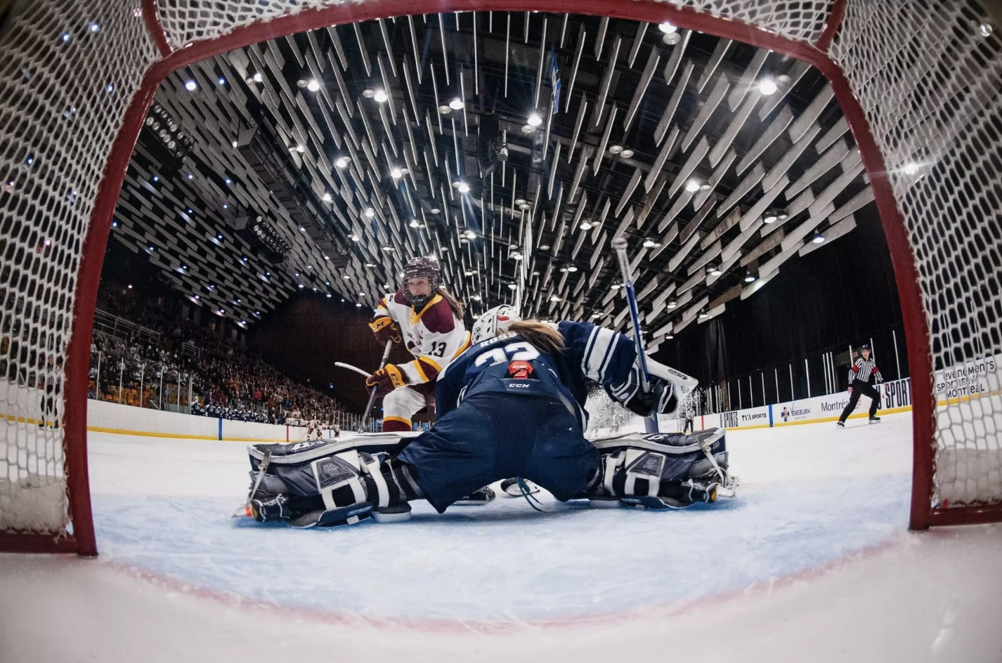 A shot from inside the net as Ross makes a left leg save from her knees. She is wearing a navy Mount Royal uniform.
