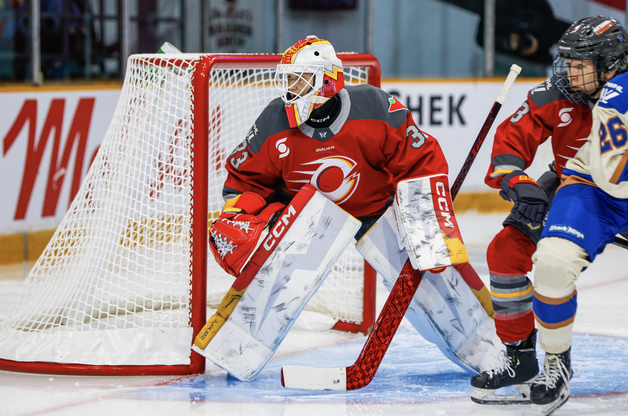Phillips looks to her right as she watches the play unfold out of frame. She is wearing a red home uniform, and mostly white pads with red and yellow stripes on the edges.