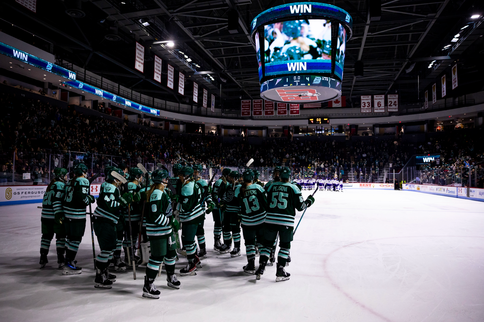 The Fleet celebrate their win with fist bumps and hugs in their defensive zone. They are all wearing green home uniforms.