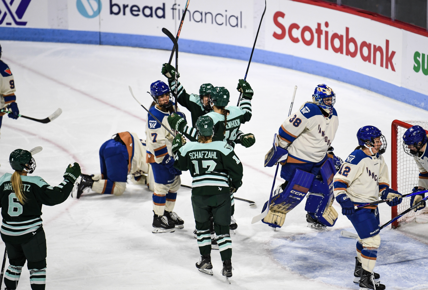 Newhook raises her arms in celebrations as her teammates come in for a group hug. They are wearing green home uniforms, while the Vancouver players scattered around the background are in cream away uniforms.