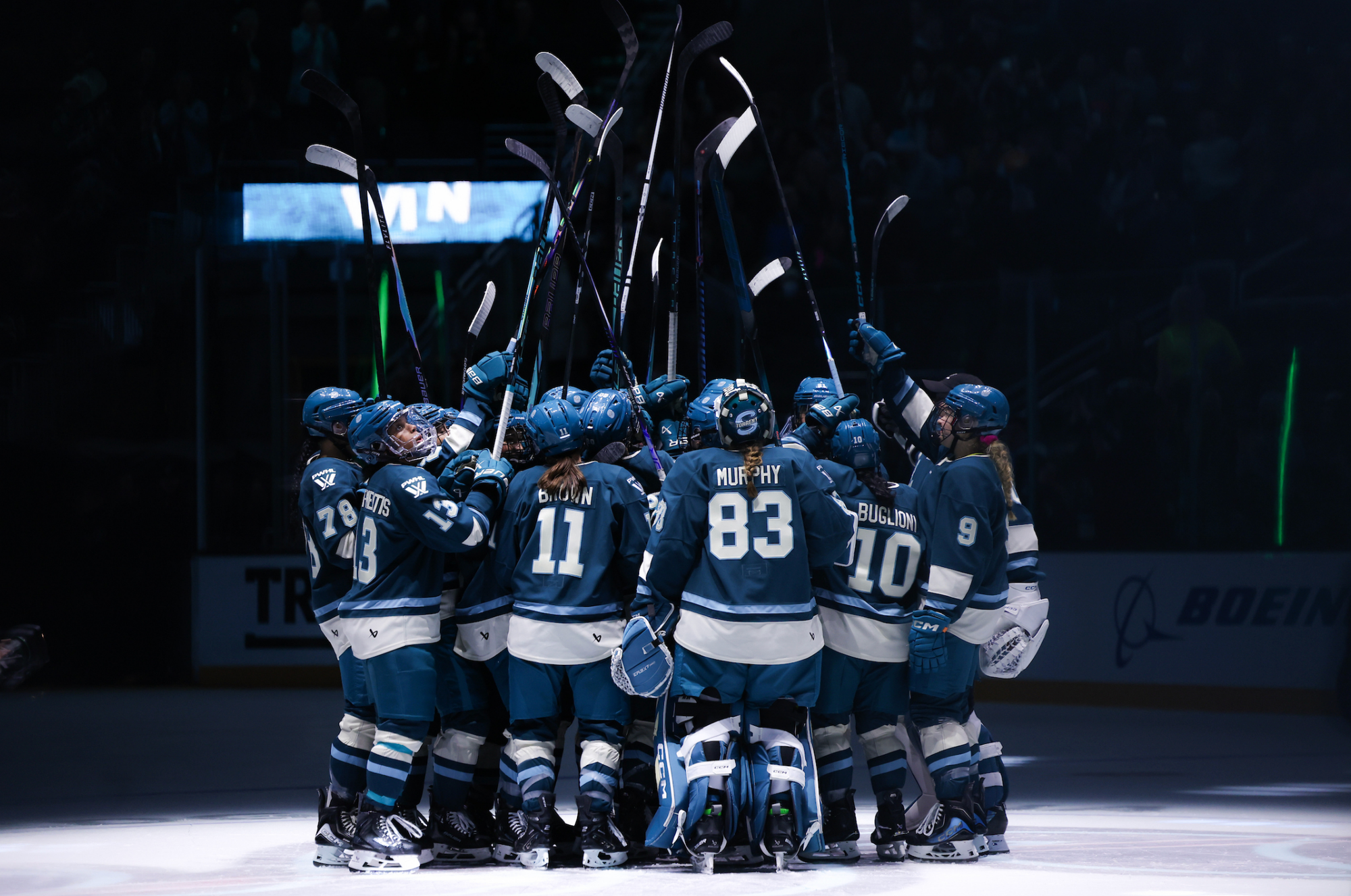 The Torrent raise their sticks as they come together for a tight group hug at center ice. They are all wearing teal home uniforms.