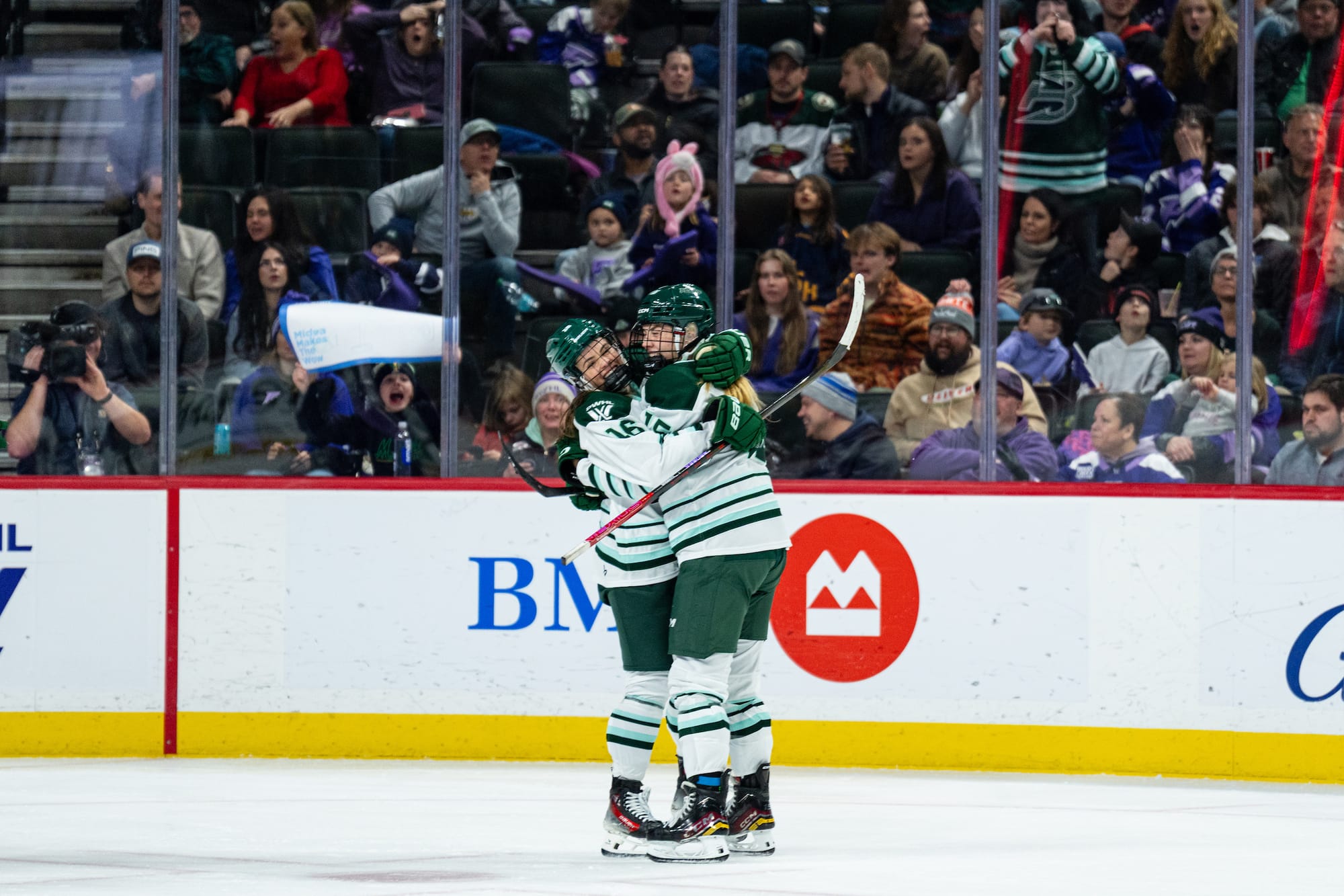 Brengman and Mobley smile and hug to celebrate a goal. They are wearing white away uniforms.