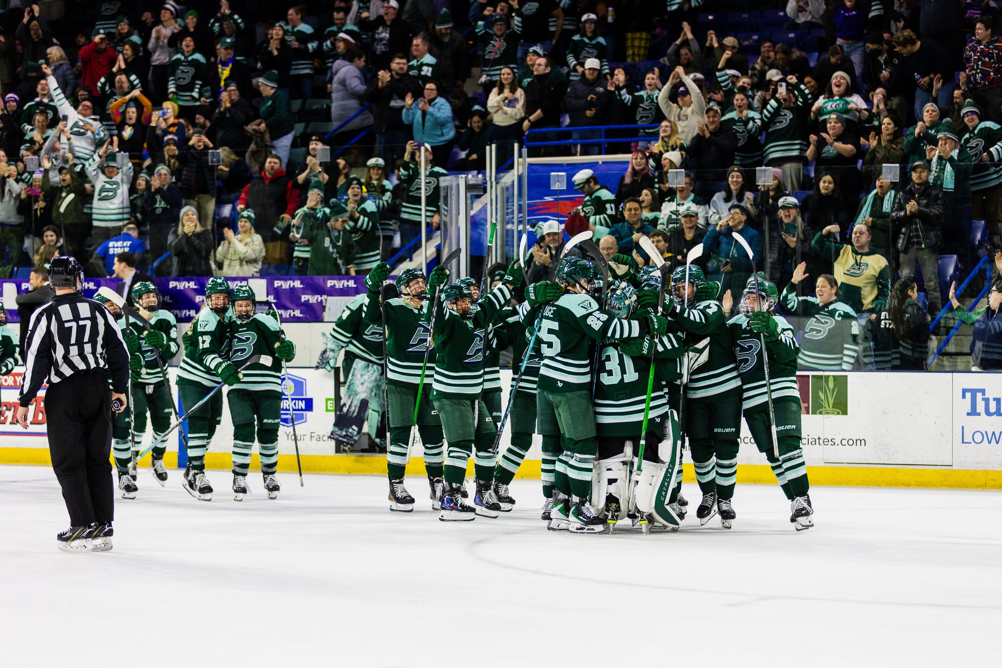 The Fleet celebrate their win over the Sirens with a big group hug. The crowd is cheering them on in the background. The Fleet players are all in green home uniforms.