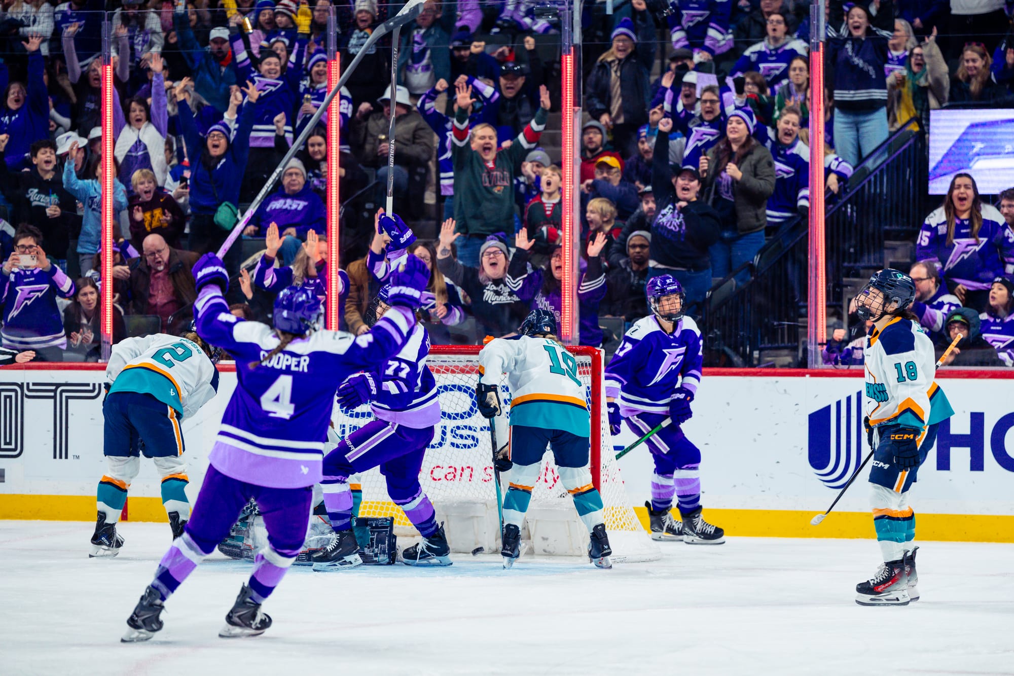 Minnesota players raise their arms in celebration after scoring a goal. The crowd is roaring in the background. The players are all in purple home uniforms. 