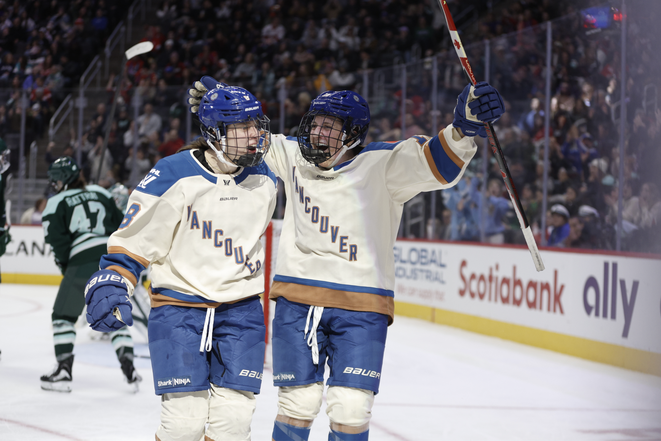 Two Vancouver players celebrate a goal by cheering and hugging. They are wearing cream away uniforms.