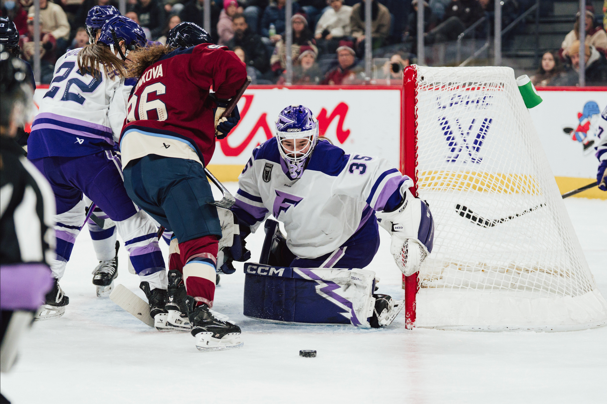 Rooney kicks a puck out while pushing off to her right. She is wearing a white away uniform.
