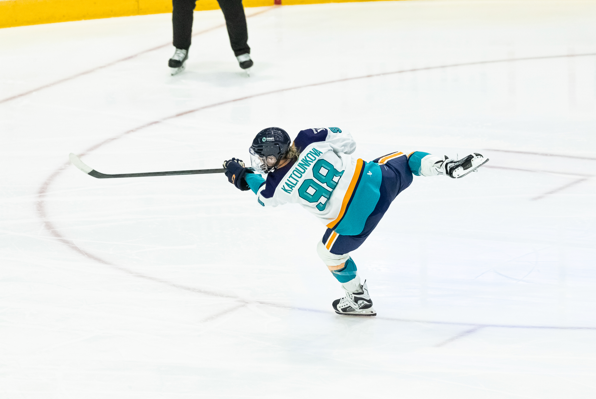 Kaltounková lifts her right leg and follows through with her stick as she fires a shot towards the goal, which is out of frame. She is wearing a white away uniform.