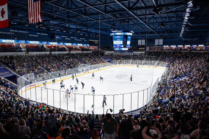 A shot taken from the top corner of the concourse, showing packed stands and the players lining up for a faceoff.